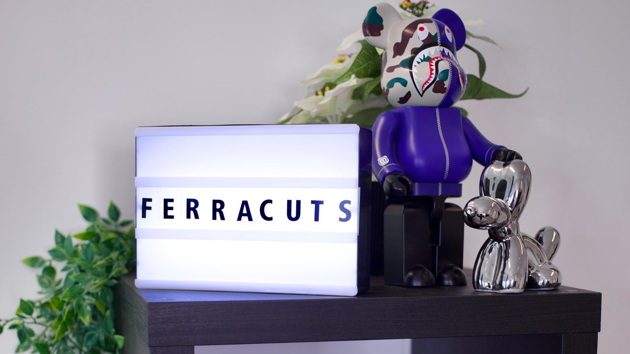 De verlichte lichtbak met FERRACUTS in de zaak, naast een paars beeldje van een beer en een plant
